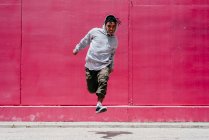 Giovani uomini ispanici che saltano vicino a un muro rosa per strada — Foto stock