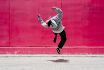 Молоді іспаномовні чоловіки стрибають біля рожевої стіни на вулиці — стокове фото