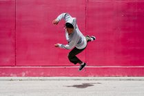 Jovens hispânicos pulando perto de uma parede rosa na rua — Fotografia de Stock