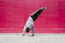 Jeunes hommes hispaniques faisant des acrobaties près d'un mur rose dans la rue — Photo de stock