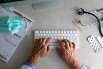 Чоловічі руки лікаря, що друкуються на клавіатурі комп'ютера на робочому столі — стокове фото