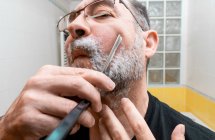 Hombre barbudo maduro afeitándose con afeitadora recta en el baño - foto de stock