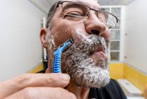 Afeitado hombre barbudo con afeitadora desechable en el baño - foto de stock