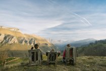 Bambini in abiti casual seduti su panchine di legno sulla collina verde remota e godendo della vista durante la visita in Spagna — Foto stock