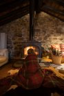 Cuddling kid wrapped in cozy tartan plaid sitting on wooden floor near burning fireplace and looking at fire in stone house in Cantabria — Stock Photo