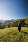 Visão traseira do caminhante feminino anônimo abraçando crianças enquanto estava em pé no prado verde e observando a paisagem pitoresca de montanhas no dia ensolarado na Cantábria — Fotografia de Stock