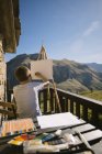Vista posteriore del ragazzo senza volto in t shirt bianca seduto al cavalletto sulla pittoresca veranda della casa di campagna e disegno immagine in Cantabria — Foto stock