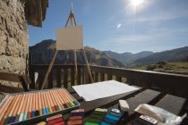 Set of colorful pencils and various painting tools placed on wooden table near easel with canvas on sunny terrace of old stone house in Spain — Stock Photo