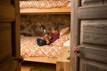 Criança concentrada em roupa casual sentada em cama confortável no quarto e jogando ukulele enquanto relaxa em casa na Cantábria — Fotografia de Stock