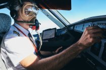 Vista lateral do aviador macho profissional na máscara de oxigênio girando o interruptor no console de controle durante a operação de aeronaves contemporâneas durante o voo — Fotografia de Stock