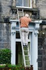 Hombre anónimo mayor reparando la puerta de la vieja mansión - foto de stock