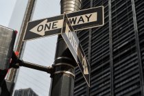 Снизу односторонние дорожные знаки на перекрестке с современными высотными зданиями на фоне Нью-Йорка — стоковое фото