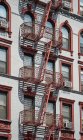 Desde abajo de la fachada del edificio de apartamentos clásico con escalera de incendios de metal en la calle de la ciudad de Nueva York - foto de stock