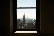 Vista de la ciudad de Nueva York con rascacielos y Empire State Building visto desde una ventana estrecha a la luz del sol - foto de stock
