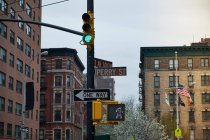 Low angle of signpost with various road signs and green traffic light in old district of New York City with weathered buildings on background — Stock Photo