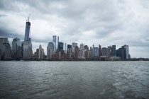 Arranha-céus contemporâneos de Nova York vistos do rio contra o céu azul nublado em dia ensolarado — Fotografia de Stock