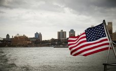 National flag of USA waving on pole of floating vessel against cloudy sky near New York City coast — Stock Photo