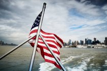 Государственный флаг США машет на полюсе плавучего судна против облачного неба вблизи побережья Нью-Йорка — стоковое фото