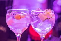 Gläser mit frischen alkoholtonischen Cocktails mit Eiswürfeln und Früchten vor verschwommenem Neonhintergrund — Stockfoto