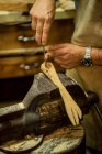 Анонимный плотник в фартуке, использующий стамеску для проделывания отверстий в деревянном продукте, зажатый в рабочей скамейке во время работы в мастерской — стоковое фото