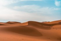 Paysage désertique minimaliste avec des dunes de sable sous un ciel nuageux bleu — Photo de stock