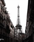 Монохромный фасад высокой Эйфелевой башни в конце узкой улочки со старыми красивыми монументальными зданиями на фоне ярко-белого неба в Париже — стоковое фото