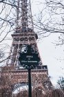 Vista panoramica del cartello stradale in acciaio nero contro la torre Eiffel sfocata e rami d'albero senza foglie nella calda giornata primaverile a Parigi — Foto stock
