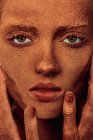 Молода красива жінка з шоколадним порошком на обличчі торкається шкіри і дивиться на камеру — стокове фото