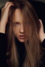 Schöne junge Frau blickt in die Kamera und zerzaust lange blonde Haare vor schwarzem Hintergrund — Stockfoto