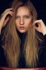Beautiful young lady looking at camera and tousling long blond hair against black background — Stock Photo