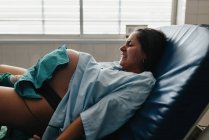 Затягнута жіноча ручка хапає і гризе біль, народжуючи дитину на медичному кріслі в сучасній лікарні — стокове фото