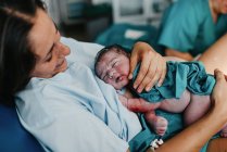 Alto ángulo de alegre mujer adulta abrazando al recién nacido cubierto de sangre después de dar a luz en la sala de partos del hospital contemporáneo - foto de stock