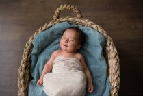 Vista superior do bebê recém-nascido envolto em pano deitado em cobertor macio e dormindo em cesta de vime no chão em casa — Fotografia de Stock