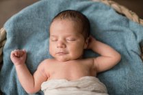 Blick von oben auf ein Neugeborenes, das in ein Tuch gewickelt auf einer weichen Decke liegt und zu Hause in einem Weidenkorb auf dem Boden schläft — Stockfoto