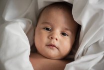 Vista superior do bebê bonito envolto em tecido branco olhando para a câmera em casa — Fotografia de Stock