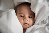 Draufsicht des niedlichen Säuglings in weißen Stoff gehüllt, der zu Hause in die Kamera schaut — Stockfoto