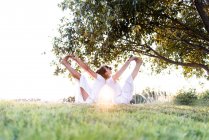 Seitenansicht eines entspannten Paares, das in Yogaposition sitzt und die Beine hochhebt und die Hände an den Füßen hält, während man sich auf den Rücken stützt — Stockfoto