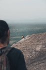 Вид ззаду на врожай безликий чоловічий турист, що стоїть на скелястій горі і фотографує гірського орла, що сидить на краю скелі в літній вечір — стокове фото