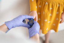 De arriba vista del médico anónimo en guantes de látex usando el puño de dedo para examinar la presión arterial de la niña en vestido amarillo casual - foto de stock