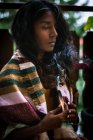 Giovane donna etnica spirituale con gli occhi chiusi in abiti tradizionali che reggono incenso di salvia ardente con fumo e meditando all'aperto — Foto stock