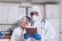 Доктор пояснює медичну інформацію старшому пацієнту вдома під час карантину коронавірусу — стокове фото