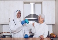 Mujer mayor alegre con cuidador bebiendo té en la cocina durante la cuarentena - foto de stock