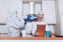 Empleado de atención domiciliaria ayudando a cliente senior en casa durante cuarentena - foto de stock