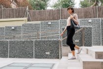 Femme brune heureuse adulte en tenue décontractée et écharpe grise marchant sur des escaliers en béton le jour ensoleillé et regardant ailleurs — Photo de stock