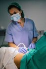 Médecin féminin dans un masque stérile et un gant bleu à l'aide d'un scanner à ultrasons tout en examinant la femme enceinte et en regardant l'écran d'ordinateur à l'hôpital — Photo de stock