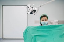 Жінка-лікар у блакитній формі та стерильній масці, яка вивчає невпізнаваного пацієнта на гінекологічному кріслі в клініці фертильності — стокове фото