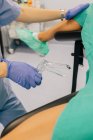 Médica sem rosto em luvas azuis e uniforme com espelho ginecológico de plástico examinando paciente anônimo em capas de sapato deitado na cadeira na clínica de fertilidade — Fotografia de Stock