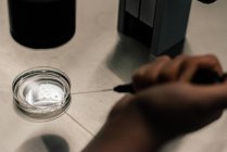 Выше врач в медицинской маске и однородной инъекционной яйцеклетке на чашке Петри и обследование клетки через микроскоп в лаборатории современной клиники фертильности — стоковое фото