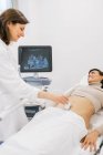 Médico de cultivos haciendo ecografía a la mujer embarazada feliz durante el trabajo en la clínica de fertilidad contemporánea - foto de stock