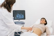 Crop medico facendo ecografia alla donna incinta felice durante il lavoro nella clinica di fertilità contemporanea — Foto stock